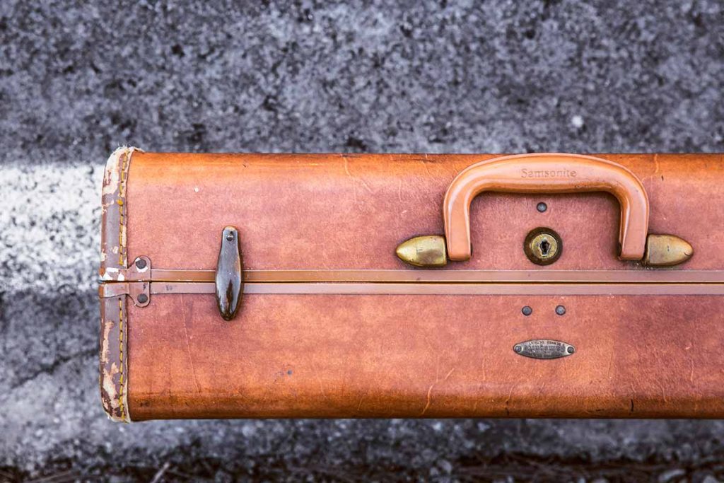 Old wooden suitcase with rusty lock and handle on asphalt surface.